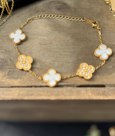Gold bracelet with clover-shaped charms on a wooden surface